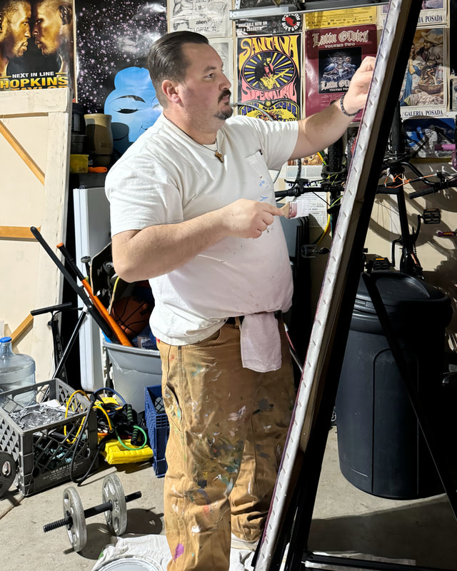 Photo of Chicano artist Roberto Valdes Sanchez standing with a paint brush in front of a large canvas he is painting.