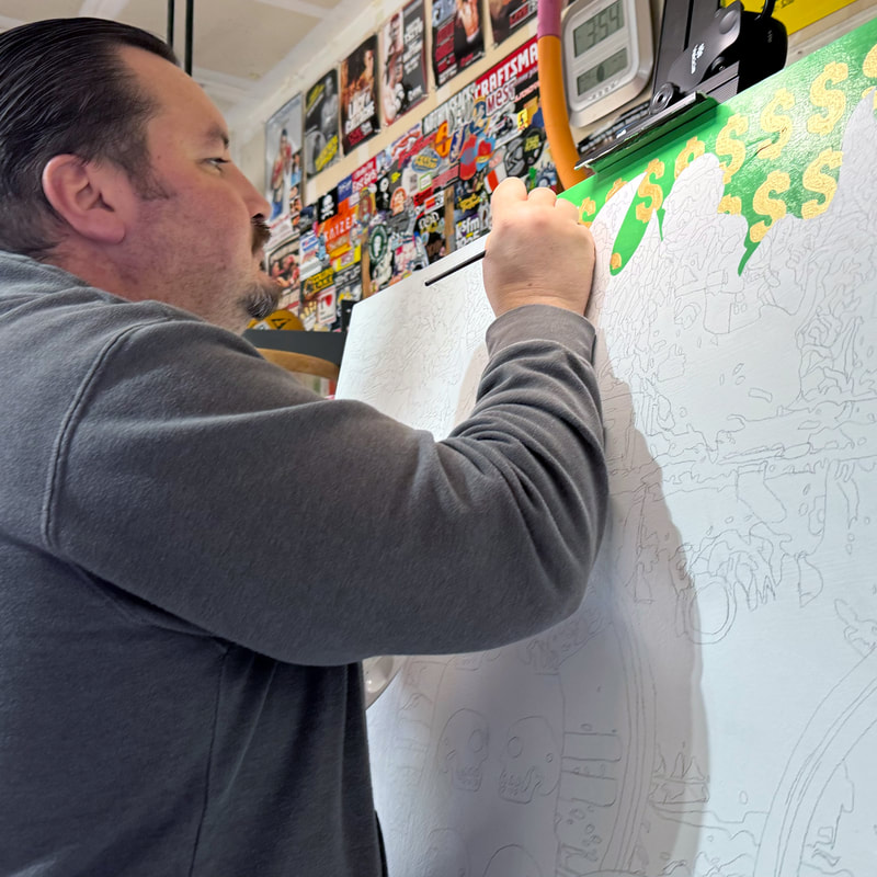 Photo of Chicano artist Roberto Valdes Sanchez painting gold dollar signs on a large canvas.